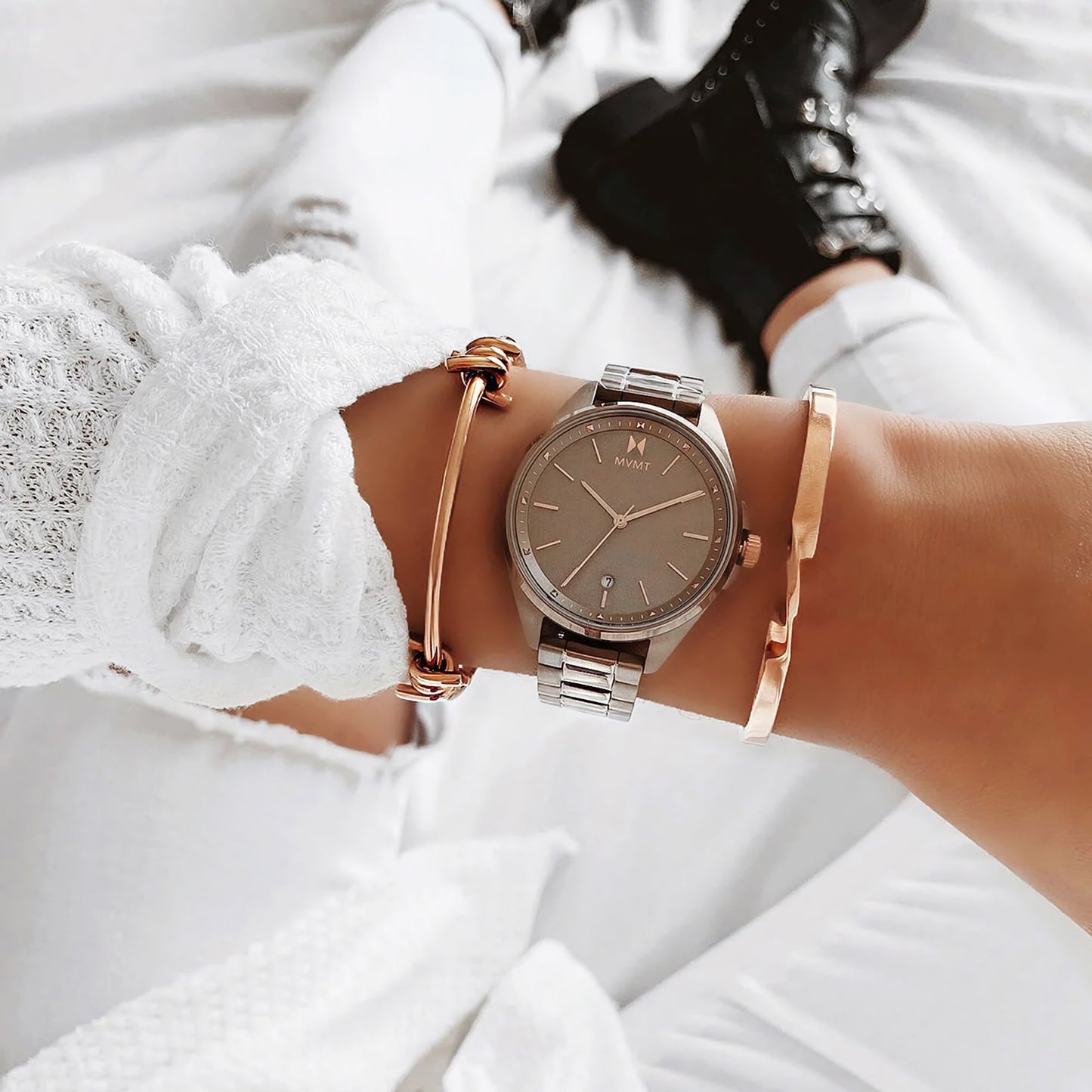 Close-up of MVMT's Coronada Moonliner watch with gold bangles, highlighting mixed metals over a white knit sweater.