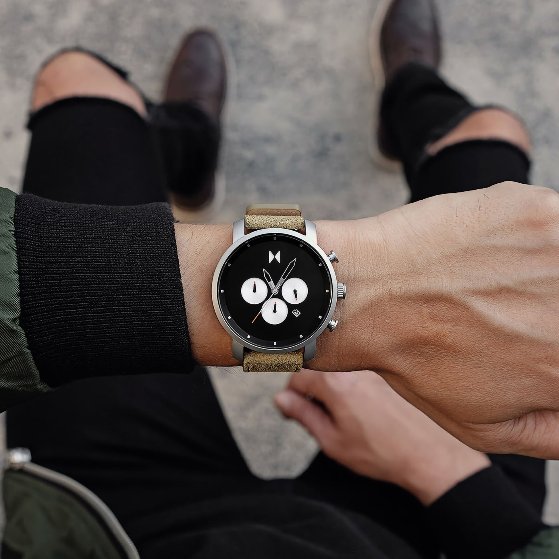 Someone wearing an MVMT Chrono 45 Moss Green watch, viewed from above, sitting with legs crossed.