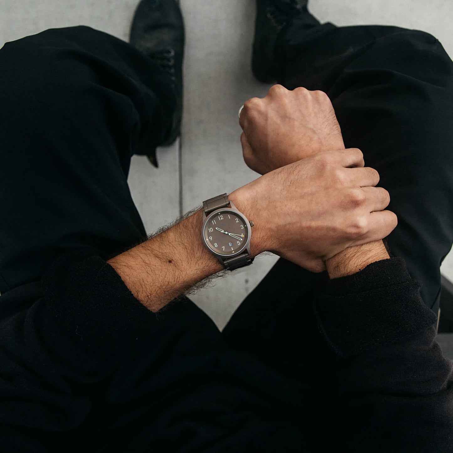 Person wearing a MVMT Field Taupe Date Explorer, dressed in black, checks its water resistance while seated.