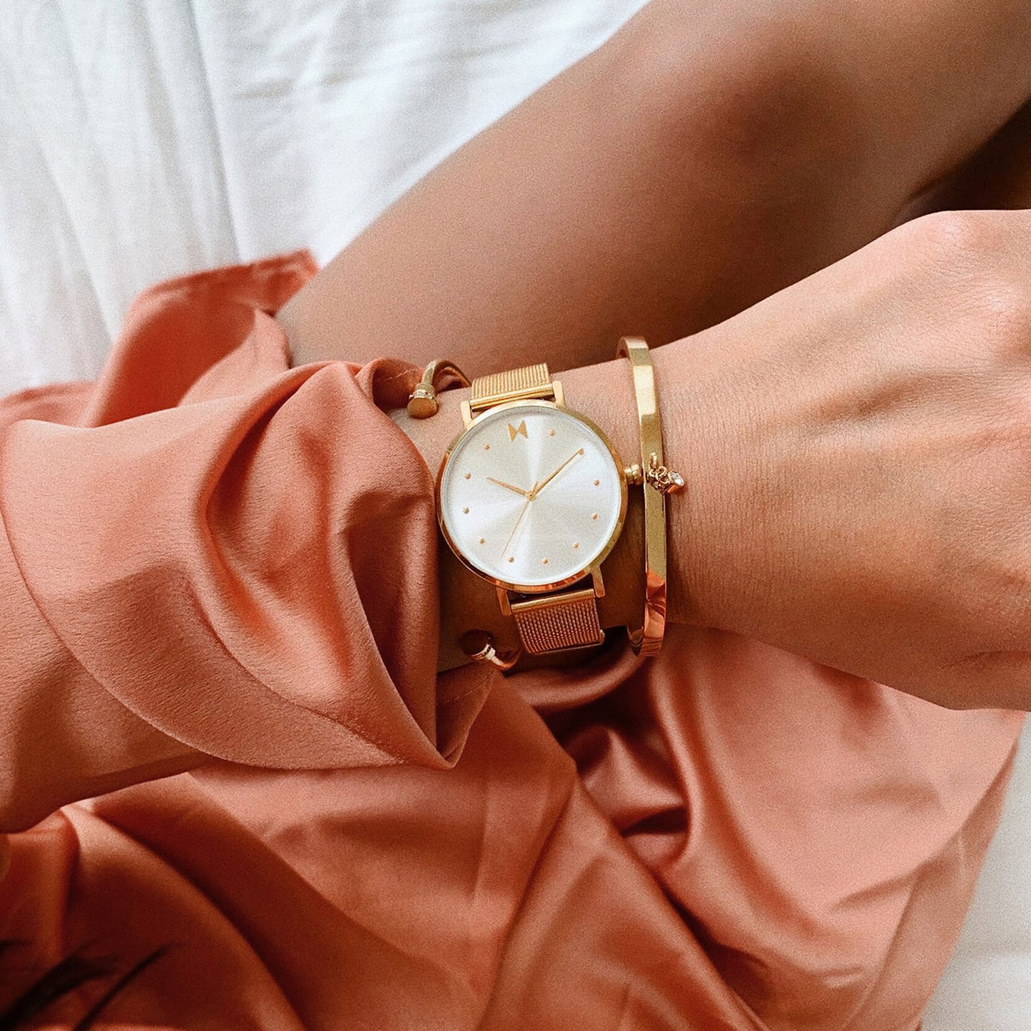 Close-up of a person wearing the MVMT Dot Flash Gold Ladies watch and bracelet on their lap in a peach dress.