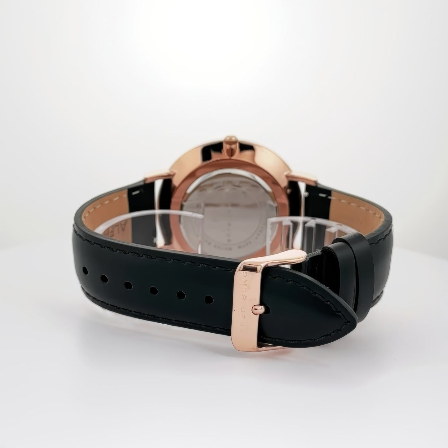 Alfred Sung Metropolitan watch: rosegold case, black leather strap, white dial; elegantly displayed on a white surface.