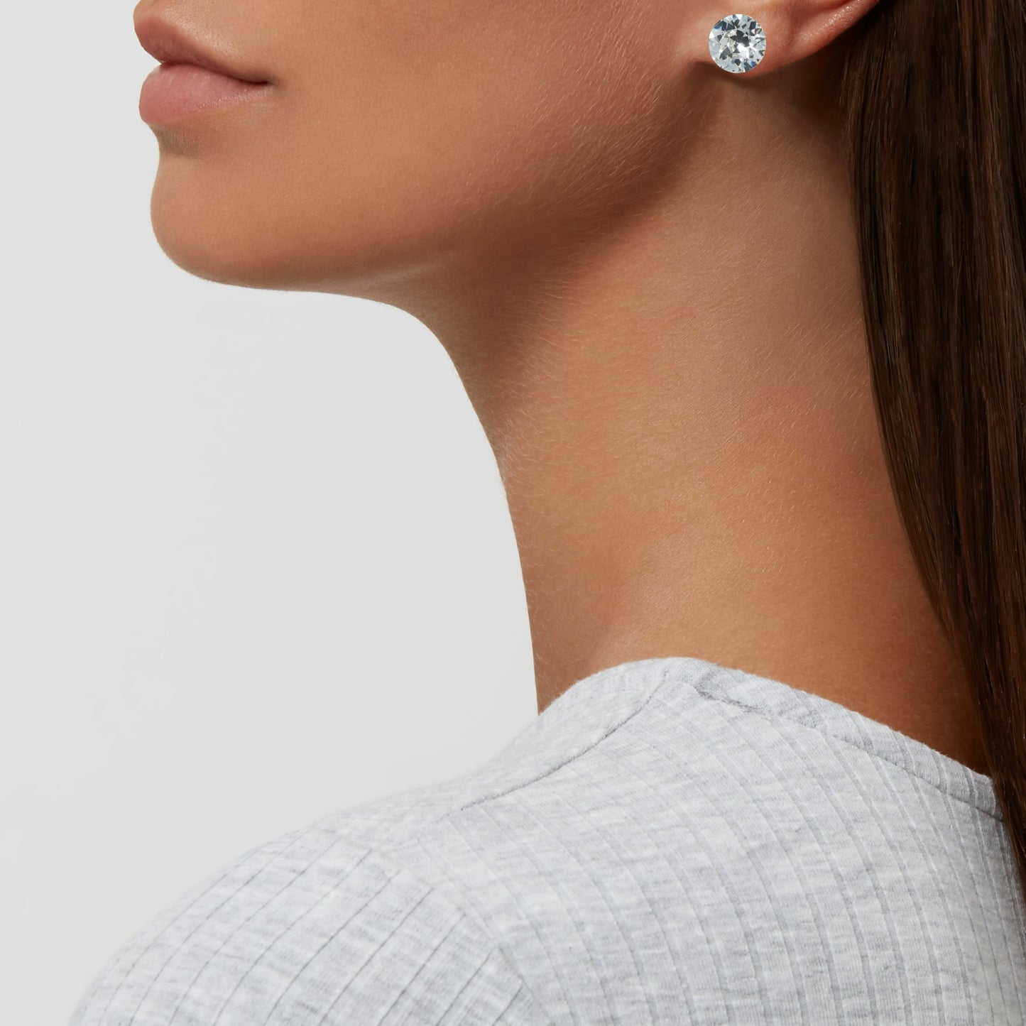 Close-up of a person wearing Aura's Stud Earrings With Crystals, highlighting a clear gemstone set in 18k gold, side profile against a light background.