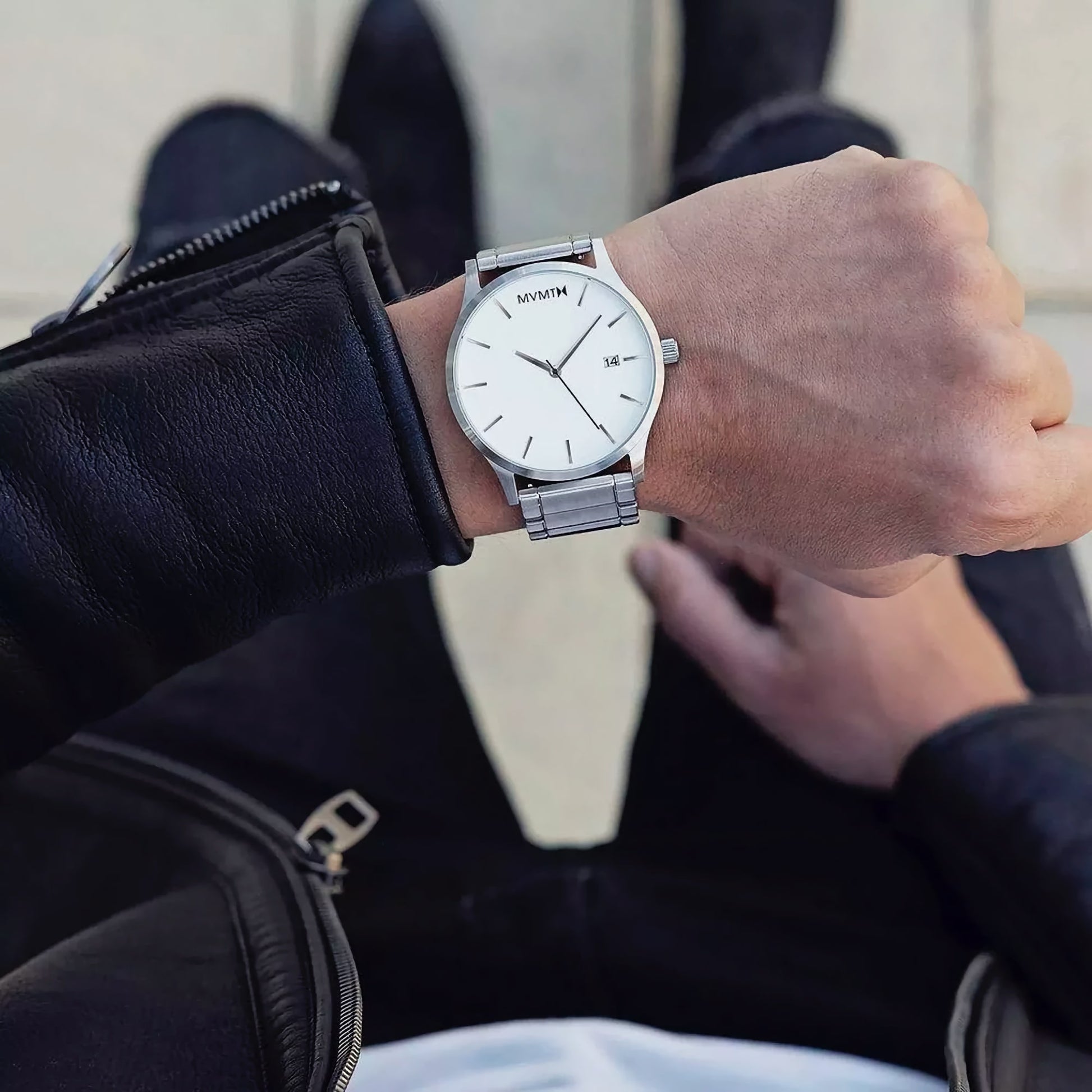A man in a black leather jacket checks the minimalist MVMT Classic White Silver Men's Watch on his wrist.