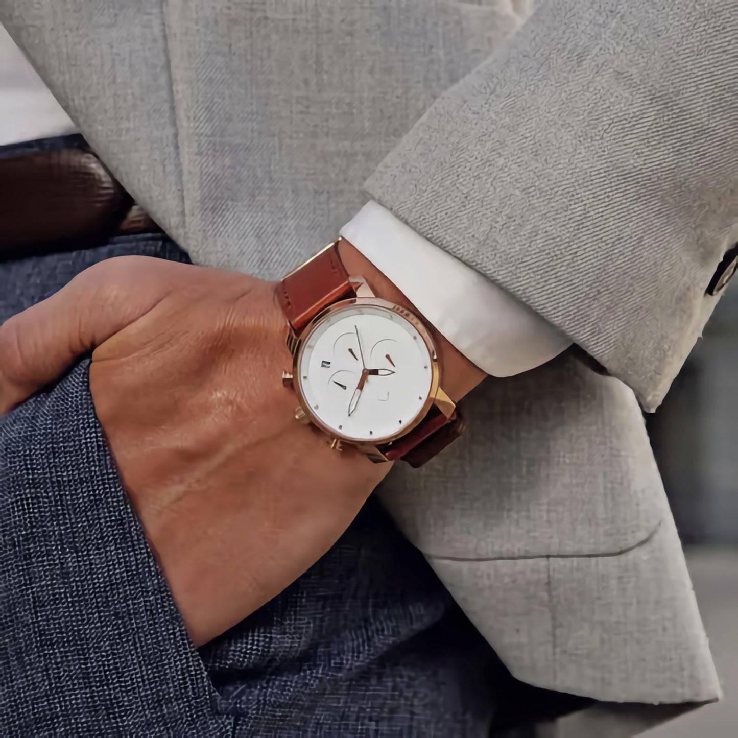 Close-up of a wrist wearing the MVMT Chrono Rose Gold Natural Tan watch, hand in gray pants pocket.