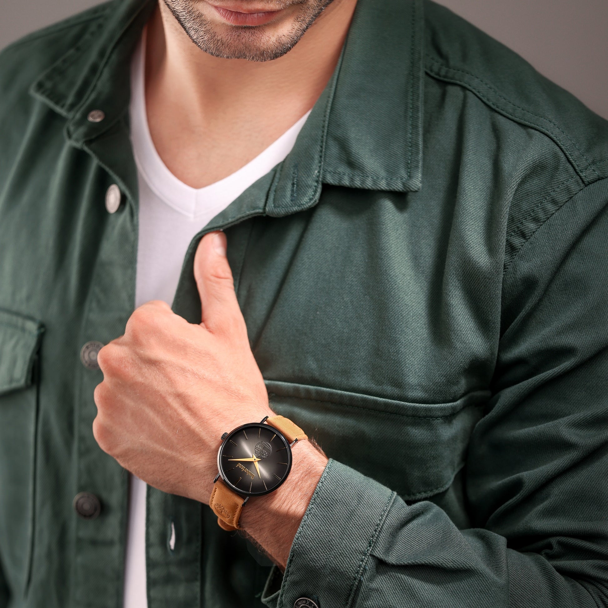 Man in a green jacket and white shirt showcases the Timberland Rangeley watch with black-plated steel & brown leather strap.