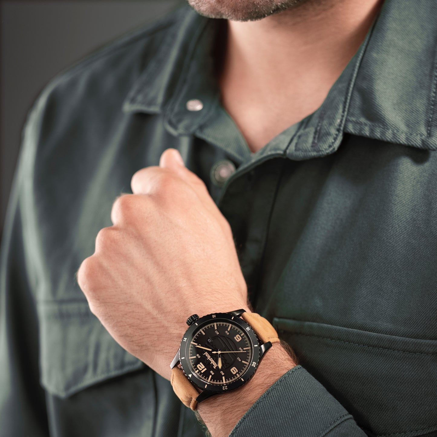 Person wearing a dark green shirt and Timberland's Ashmont watch, ionic-plated steel with a tan leather strap, showing the time.
