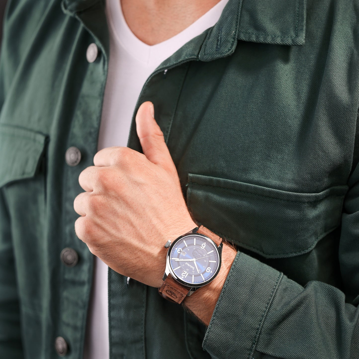 Person in a green jacket gives a thumbs up, showing off the Timberland Blake watch with its leather strap and blue dial.