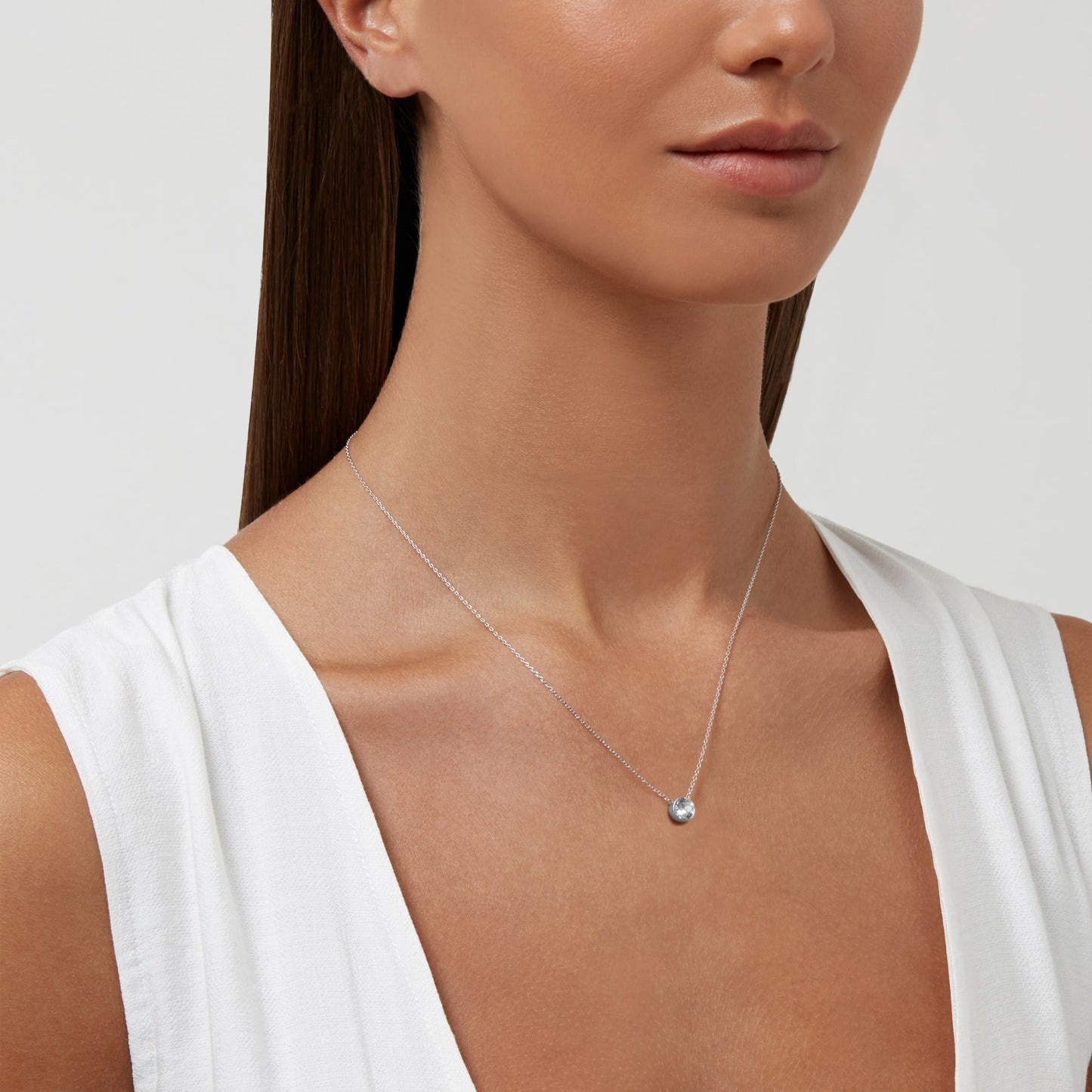 A woman wearing a Pendant Necklace With Crystals by Aura, dressed in a sleeveless white top.