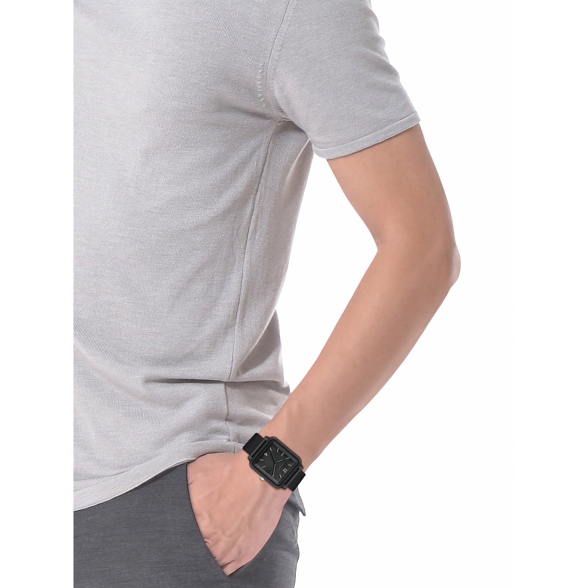 A man wearing a grey t-shirt and gray pants showcasing his Lacoste.12.12 Studio 3 Hands Watch Black Silicone in a Studio setting.
