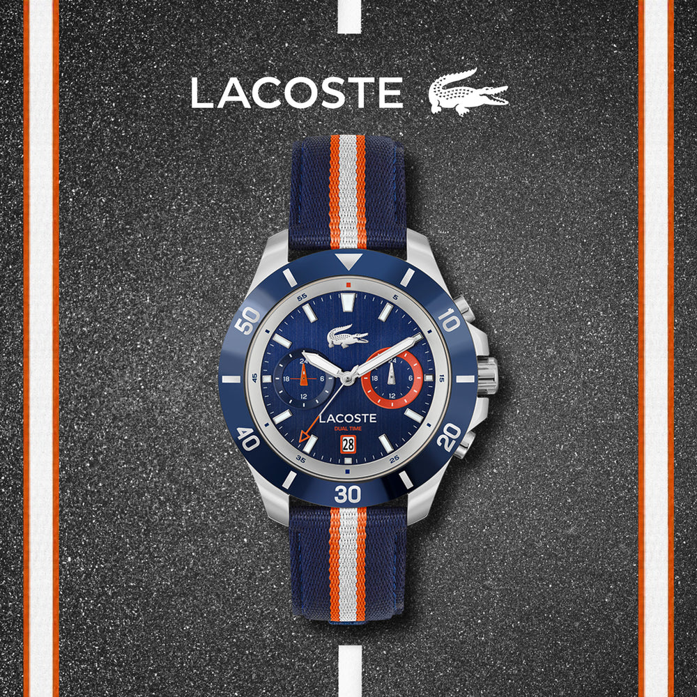Lacoste watch with a blue dial, silver bezel, and orange-striped blue nylon strap on a road-like background.